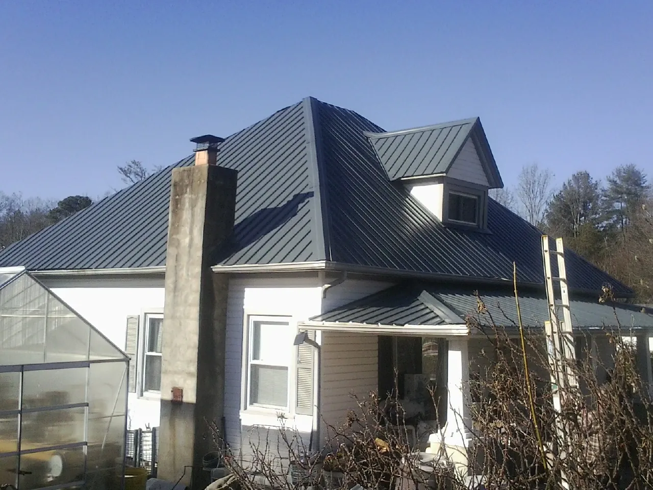 Dark blue standing seam metal roof on a white farmhouse with dormer — Slate & Tile Roof Repair by Roofing Brothers in Walnut Grove