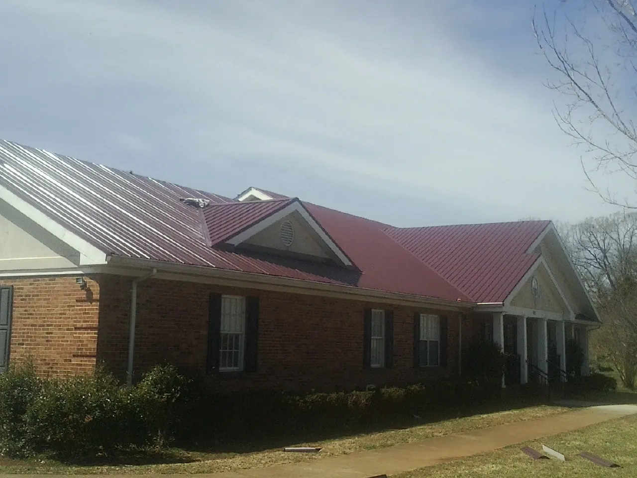 Red metal roof with gabled entries on a long brick building, from a Hail Damage Roof Repair job in Walnut Grove