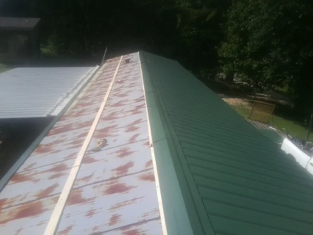 Old rusted panels beside newly installed green metal roofing — Wind Damage Roof Repair by Roofing Brothers in Walnut Grove
